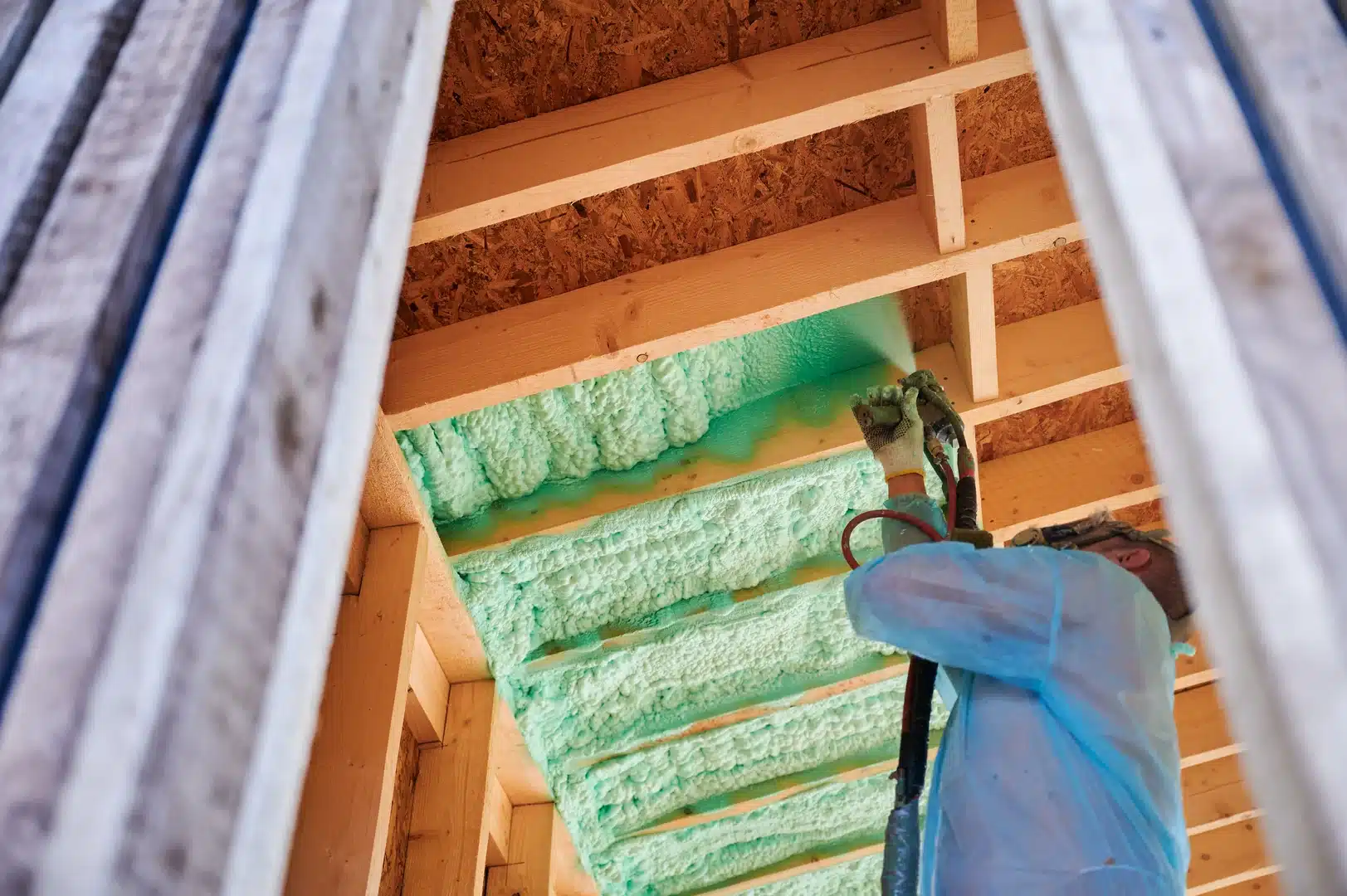 Insulation installer applying spray foam to wood framing